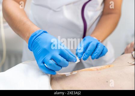 La main du médecin utilise une blessure d'infection de pansement de coton propre à l'abdomen d'un homme. Bandage pour pansement en clinique. médical Banque D'Images