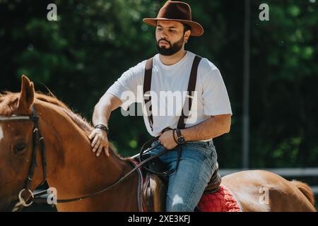 Homme confiant à cheval dans la nature, portant un chapeau de cow-boy et une tenue décontractée Banque D'Images
