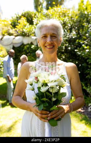 Femme senior souriante tenant un bouquet de fleurs à la cérémonie de mariage en plein air Banque D'Images