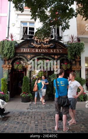 La Maison publique Cross Keys, avec de nombreuses fleurs décorant le bâtiment, les gens bavardent, fument et boivent dehors. Banque D'Images