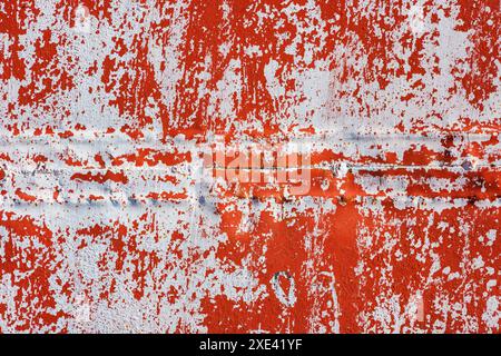 Mur en tôle d'acier rouge avec peinture blanche pelée sous la lumière directe du soleil, fond plein cadre et texture Banque D'Images