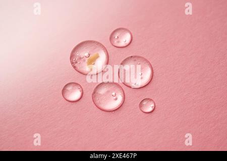 Quelques gouttes de gel cosmétique transparent sur fond rose. Banque D'Images