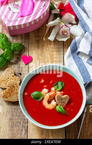 Soupe de Saint-Valentin maison, repas de fête.Soupe de tomates, purée de gazpacho avec tomates, fruits de mer servis sur une table rustique en bois. Banque D'Images