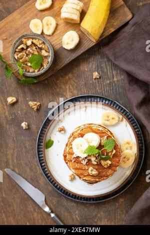 Célébration de la journée des crêpes, petit déjeuner américain. Délicieuses crêpes à la banane maison avec des noix et du caramel sur une table en bois rustique. À Banque D'Images