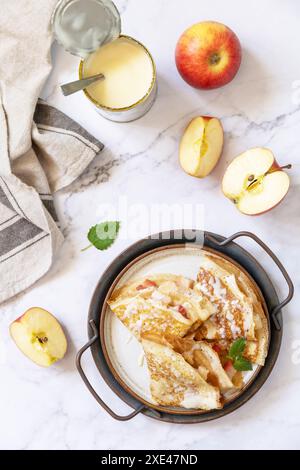 Célébration de la journée des crêpes, petit déjeuner sain. Crêpes sucrées maison avec pommes et lait condensé sur une table en marbre. Vue de dessus Banque D'Images