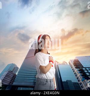 Jeune femme indonésienne pose sa main sur sa poitrine avec une expression fière, portant un bandeau de drapeau indonésien, dans une ville avec un beau soleil Banque D'Images