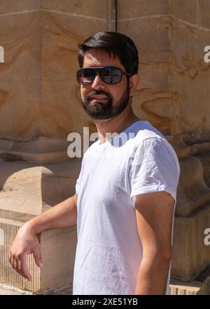 Portrait en gros plan d'un pakistanais moderne avec une barbe sombre, des vêtements légers et des lunettes de soleil. Banque D'Images