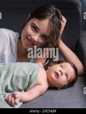 Une sœur aînée et son petit frère nouveau-né sont allongés sur le canapé. La fille regarde le bébé avec amour. Embrasse doucement le bébé. Famille, amour, Newbor Banque D'Images