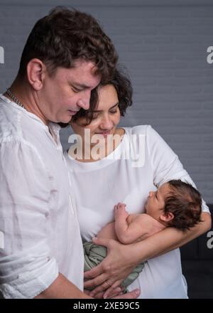 Famille heureuse avec un nouveau-né. Une mère et un père amoureux tiennent doucement leur bébé fils dans leurs bras et regardent tendrement l'enfant. Banque D'Images