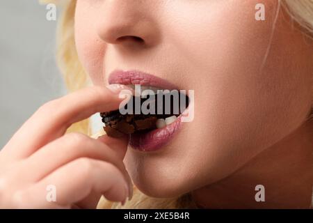 Femme blonde est avide de prendre une bouchée d'un biscuit au chocolat, se livrer à sa riche saveur et satisfaire ses envies sucrées Banque D'Images