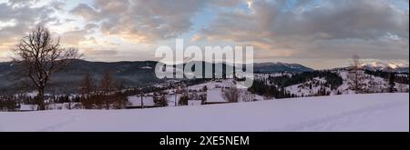 Petit village alpin et montagnes enneigées en hiver dans le premier lever du soleil autour, Voronenko, Carpates, Ukraine. Trace sur frais Banque D'Images