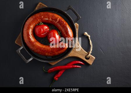 Saucisse de porc frite et tomates grillées sur une poêle en fonte noire sur une table en pierre avec espace de copie. Banque D'Images