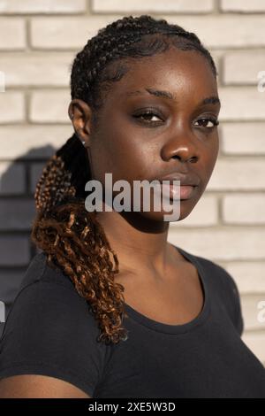 Femme africaine confiante avec cheveux tressés contre mur de briques Banque D'Images