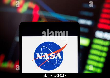 Dans cette illustration photo, l'agence américaine indépendante traitant de l'exploration spatiale et de l'aéronautique, National Aeronautics and Space Administration (NASA), logo vu affiché sur un smartphone avec un graphique d'indice boursier économique en arrière-plan. Banque D'Images