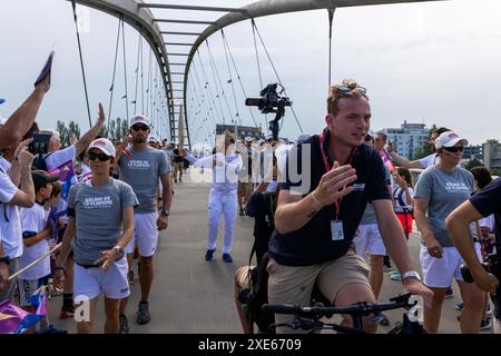 Huningue, France. 26 juin 2024. Eric Kueny porte la flamme olympique sur le pont des trois pays entre Weil am Rhein en Allemagne et Huningue en France. La flamme olympique sera allumée lors de la cérémonie d’ouverture le 26 juillet au stade de France. Avant cela, la flamme fera un arrêt à Huningue lors de sa tournée au départ de la Grèce et à travers la France. Trois porteurs de flambeaux marcheront les 600 mètres du côté allemand sur le pont des trois pays jusqu'à la place Abbatucci de Huningue. Les 33èmes Jeux Olympiques d'été auront lieu à Paris crédit : Philipp von Ditfurth/dpa/Alamy Live News Banque D'Images