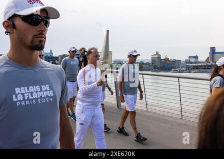 Huningue, France. 26 juin 2024. Eric Kueny porte la flamme olympique sur le pont des trois pays entre Weil am Rhein en Allemagne et Huningue en France. La flamme olympique sera allumée lors de la cérémonie d’ouverture le 26 juillet au stade de France. Avant cela, la flamme fera également une halte à Huningue lors de sa tournée au départ de la Grèce et à travers la France. Trois porteurs de flambeaux marcheront les 600 mètres du côté allemand sur le pont des trois pays jusqu'à la place Abbatucci de Huningue. Les 33èmes Jeux Olympiques d’été auront lieu à Paris. Crédit : Philipp von Ditfurth/dpa/Alamy Live News Banque D'Images