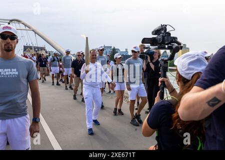 Huningue, France. 26 juin 2024. Eric Kueny porte la flamme olympique sur le pont des trois pays entre Weil am Rhein en Allemagne et Huningue en France. La flamme olympique sera allumée lors de la cérémonie d’ouverture le 26 juillet au stade de France. Avant cela, la flamme fera également une halte à Huningue lors de sa tournée au départ de la Grèce et à travers la France. Trois porteurs de flambeaux marcheront les 600 mètres du côté allemand sur le pont des trois pays jusqu'à la place Abbatucci à Huningue. Les 33èmes Jeux Olympiques d’été auront lieu à Paris. Crédit : Philipp von Ditfurth/dpa/Alamy Live News Banque D'Images