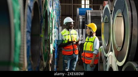 Une équipe de jeunes hommes et femmes travaillant dans un entrepôt stockant des rouleaux de tôles. Inspection des rouleaux de tôle stockés en t Banque D'Images