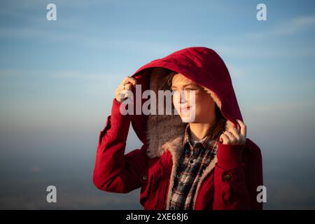 Portrait d'une belle jeune femme en manteau rouge sur fond de ciel bleu Banque D'Images