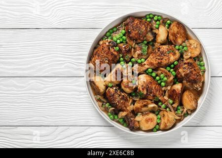 Poulet Vésuve, morceaux de poulet brun doré cuits avec pommes de terre rôties, oignon et petits pois dans une sauce au citron au vin blanc dans un plat de cuisson sur bois blanc Banque D'Images