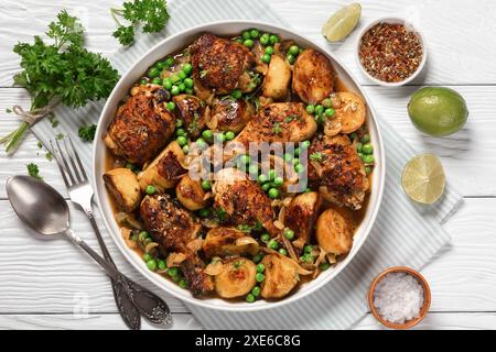 Poulet Vésuve, morceaux de poulet brun doré cuits avec pommes de terre rôties, oignon et petits pois dans une sauce au citron au vin blanc dans un plat de cuisson sur bois blanc Banque D'Images