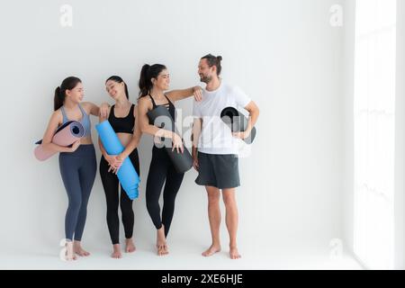 Un groupe d'athlètes féminins et masculins se sont levés et ont bavardé à l'amiable dans le studio avant de commencer le cours de yoga. Banque D'Images