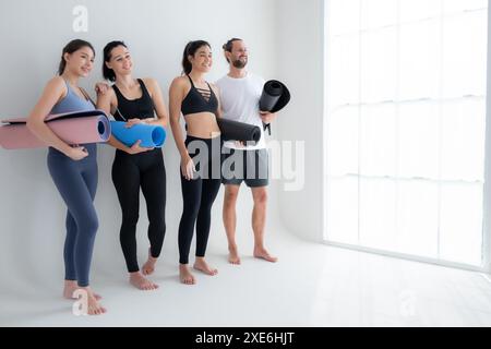 Un groupe d'athlètes féminins et masculins se sont levés et ont bavardé à l'amiable dans le studio avant de commencer le cours de yoga. Banque D'Images