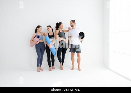 Un groupe d'athlètes féminins et masculins se sont levés et ont bavardé à l'amiable dans le studio avant de commencer le cours de yoga. Banque D'Images