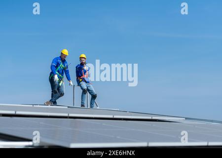 Un jeune technicien stagiaire travaillant sur des panneaux solaires a peur des hauteurs avec des ingénieurs seniors qui aident toujours Banque D'Images