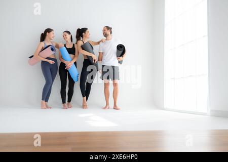 Un groupe d'athlètes féminins et masculins se sont levés et ont bavardé à l'amiable dans le studio avant de commencer le cours de yoga. Banque D'Images