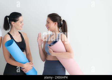 Deux jeunes athlètes féminines se sont levées et ont bavardé amicalement dans le studio avant de commencer le cours de yoga. Banque D'Images