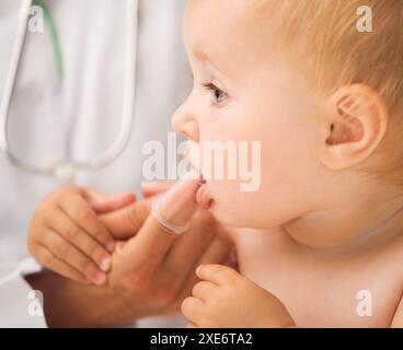 médecin nettoyant la bouche de bébé avec une brosse spéciale du bout des doigts pour les enfants Banque D'Images