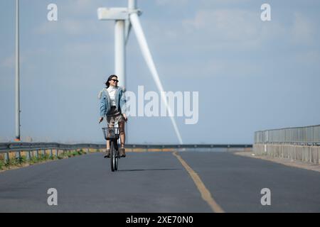 Jeune femme faisant du vélo sur une route dans un moulin à vent. Banque D'Images