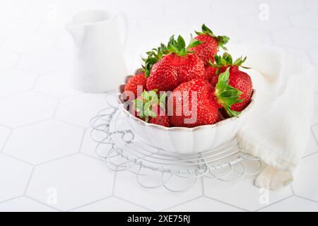 Fraises maison héritées organiques laitières dans un bol avec de la crème sur fond de bois blanc. Concept produits écologiques biologiques cultivés sur place et conservation de la nature Banque D'Images