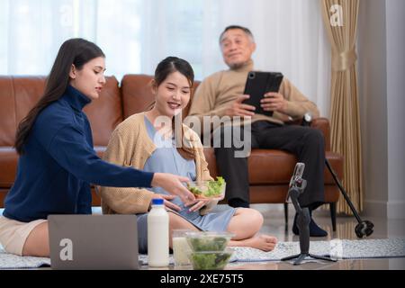 Une femme asiatique enceinte est assise par terre avec sa sœur cadette. Diffusion en direct sur les médias sociaux vendant des produits pour les mères enceintes Banque D'Images