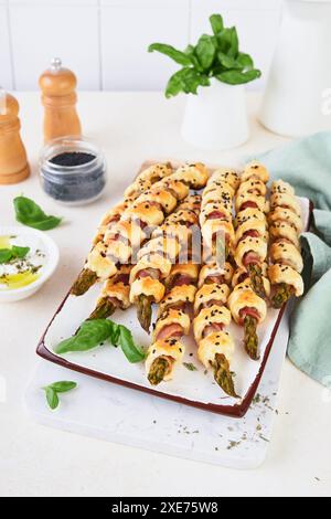 Asperges et jambon bacon feuilleté spirales ou grissini ou bâtonnets salés sur fond de table en bois clair, vue de dessus, espace copie Banque D'Images