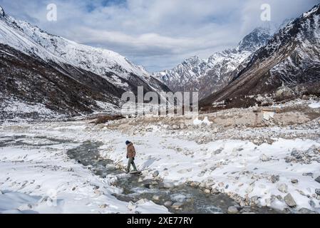 Randonneur mâle traversant une rivière gelée dans cette vallée enneigée de haute altitude, Langtang Valley Trek, Himalaya, Népal, Asie Banque D'Images