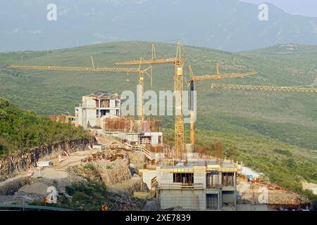 Vue sur le chantier : maisons en béton et trois grandes grues à tour sur fond de montagnes et de verdure Banque D'Images