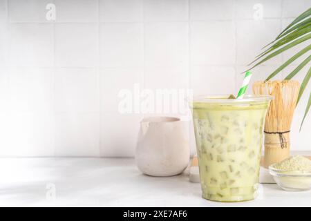 Latte matcha vert froid. Délicieux thé vert matcha glacé mélangé avec des glaçons et du lait crémeux fouetté dans un verre à latte sur fond de table blanc Banque D'Images