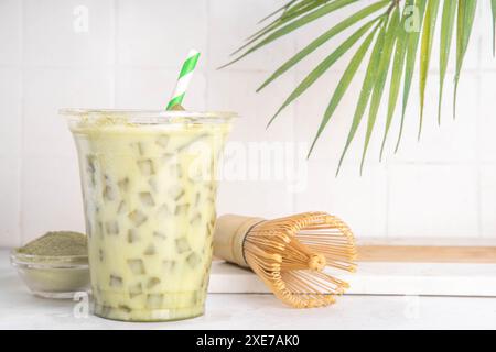 Latte matcha vert froid. Délicieux thé vert matcha glacé mélangé avec des glaçons et du lait crémeux fouetté dans un verre à latte sur fond de table blanc Banque D'Images