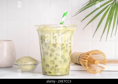 Latte matcha vert froid. Délicieux thé vert matcha glacé mélangé avec des glaçons et du lait crémeux fouetté dans un verre à latte sur fond de table blanc Banque D'Images