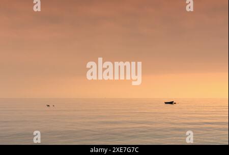 Petit bateau au nachor dans un océan calme au coucher du soleil Banque D'Images