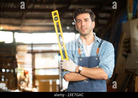 Portrait d'un charpentier tenant un niveau à bulle dans son atelier. Banque D'Images