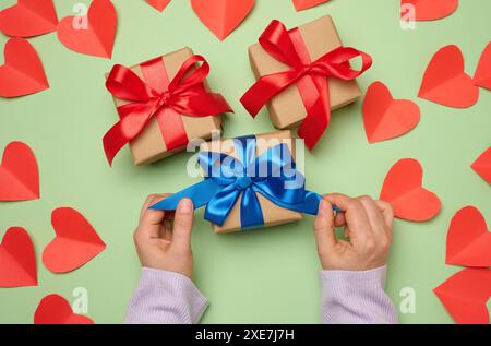 Main de femme tenant une boîte cadeau enveloppée dans un ruban de soie rouge sur un fond vert Banque D'Images