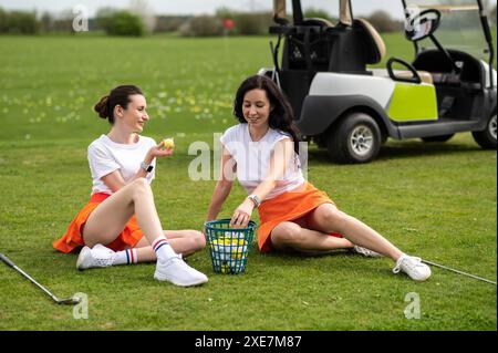 Belles filles de golfeurs assis près de son transport sur le champ vert Banque D'Images