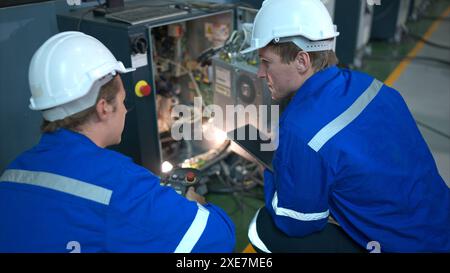 Technicien travaillant sur l'armoire de commande électrique du bras robotique, arrière-plan industriel des bras robotiques Banque D'Images