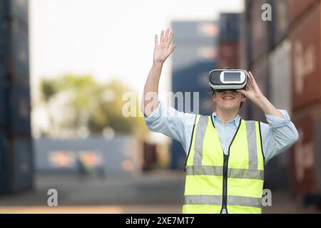 Femme portant un casque de réalité virtuelle ou des lunettes 3D pour contrôler le travail dans un entrepôt de conteneurs. Banque D'Images