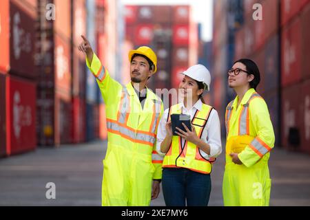 Groupe d'ingénieurs travaillant avec un ordinateur portable dans la cour de conteneurs. Il s'agit d'un entrepôt de transport et de distribution de marchandises. Banque D'Images