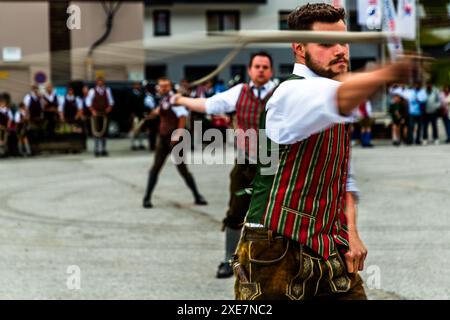 Deux hommes en gilets rayés rouge et vert font claquer leurs fouets en même temps lors de la coutume du Sonnwendklöcken à Nessler près de Großarl dans la vallée de Großarl, Salzbourg, Autriche. Une personne en arrière-plan se prépare pour le même mouvement. Banque D'Images