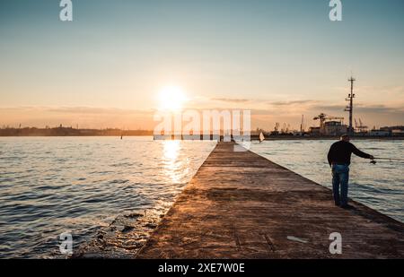 Jetée près du port de mer au coucher du soleil - perspective décroissante. Soleil couchant bas sur la baie et silhouettes de pêcheurs. Banque D'Images